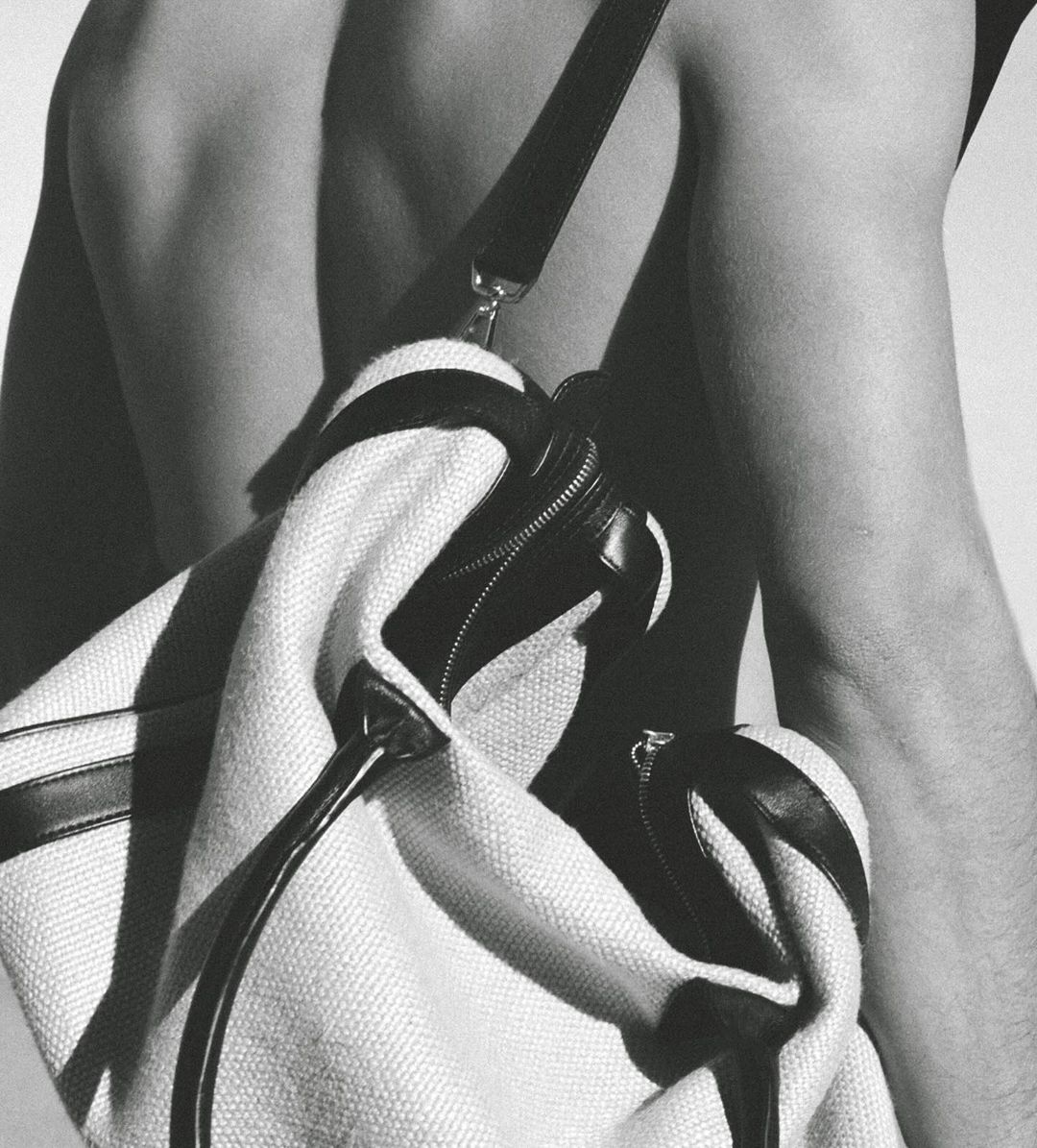Black and white studio shot of a light-colored duffel bag with black accents slung over a person's bare shoulder and back.