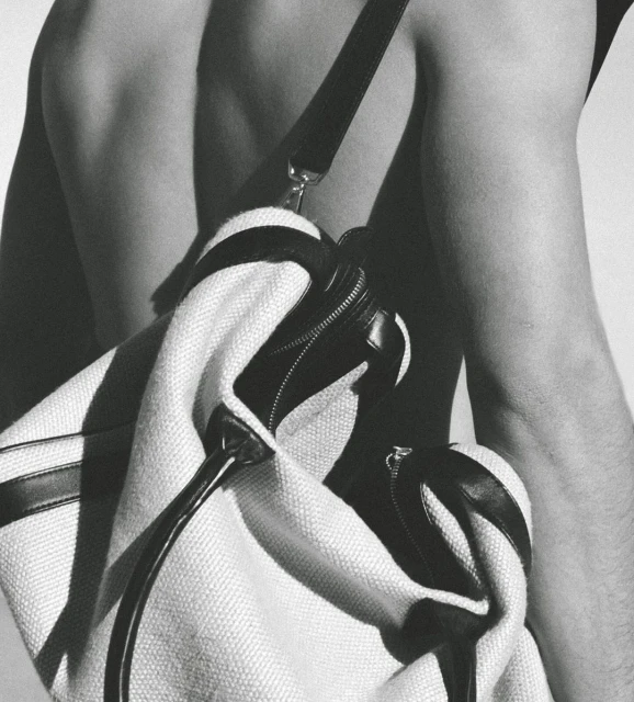 Black and white studio shot of a light-colored duffel bag with black accents slung over a person's bare shoulder and back.