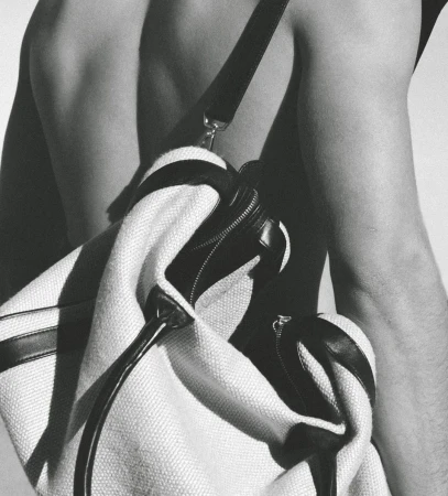 Black and white studio shot of a light-colored duffel bag with black accents slung over a person's bare shoulder and back.