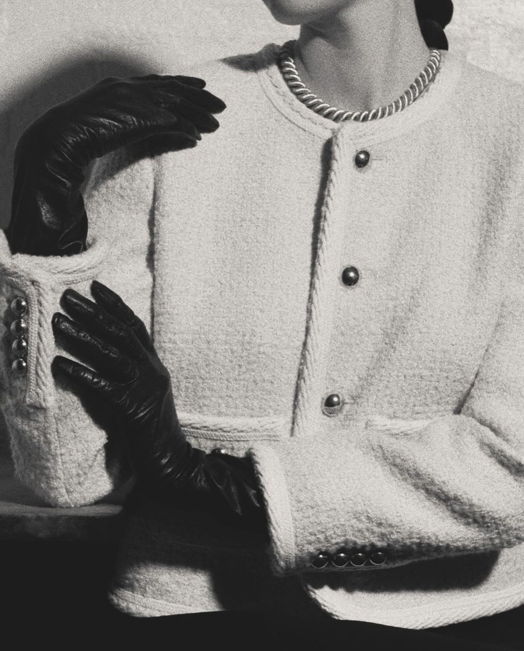 Monochromatic fashion shot of a woman in a boucle jacket with black gloves, posing in a studio with a blurred background and soft lighting.
