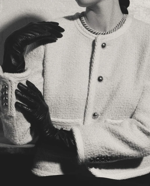 Monochromatic fashion shot of a woman in a boucle jacket with black gloves, posing in a studio with a blurred background and soft lighting.