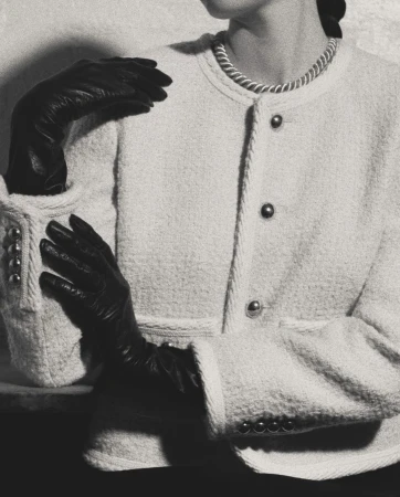 Monochromatic fashion shot of a woman in a boucle jacket with black gloves, posing in a studio with a blurred background and soft lighting.