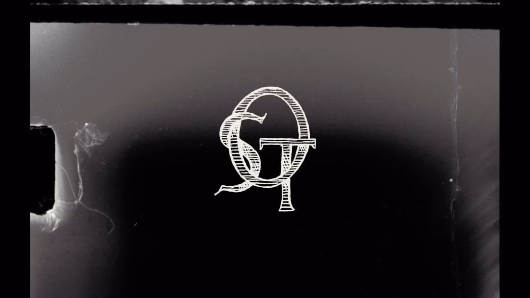 Monochromatic background with a white monogram featuring intertwined letters G and T, presented in a stylized and vintage design.