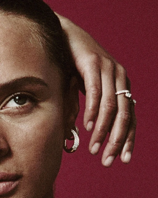 Close-up on an adult woman's face and hand, featuring diamond jewelry against a dark pink background in a beauty and fashion editorial.