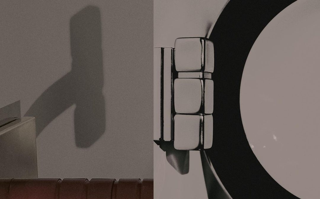 Abstract composition featuring a metallic cubic structure with a round element against a gray wall and a distinct shadow.