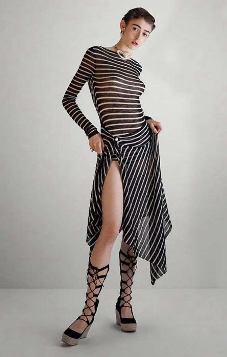 Full-length portrait of an adult woman wearing a striped top, skirt, and lace-up heels, posing in a neutral-toned indoor setting.