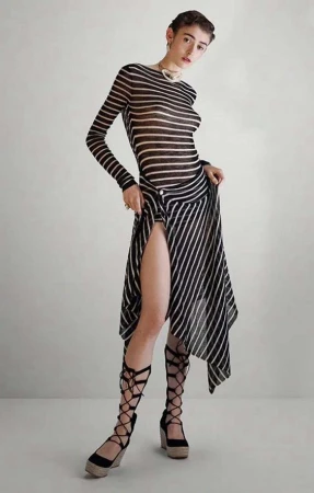 Full-length portrait of an adult woman wearing a striped top, skirt, and lace-up heels, posing in a neutral-toned indoor setting.