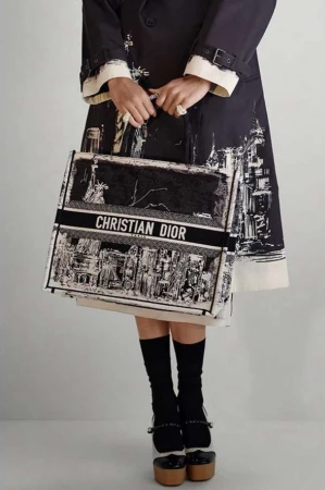 Fashion shot: Woman with Christian Dior tote bag, wearing black and white coat, knee socks, and platform heels in studio.
