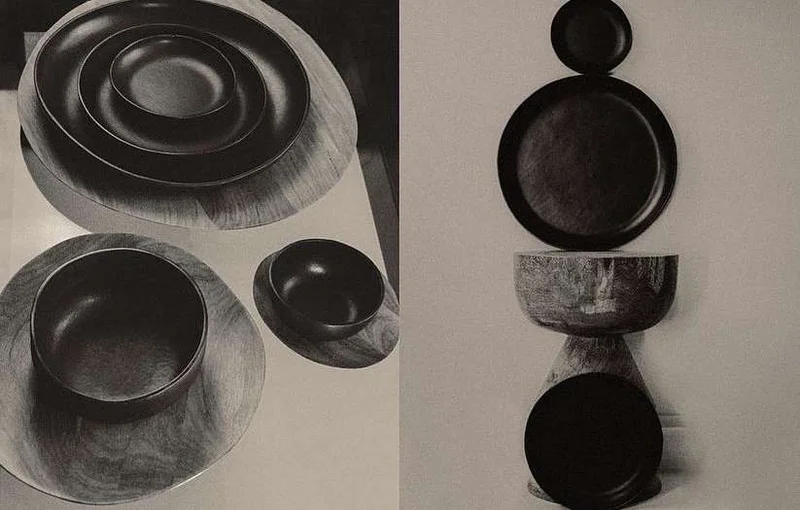 Monochrome still life photo showing dark ceramic bowls and plates arranged on wooden platters in Paris by Anastasiia Duvallie.