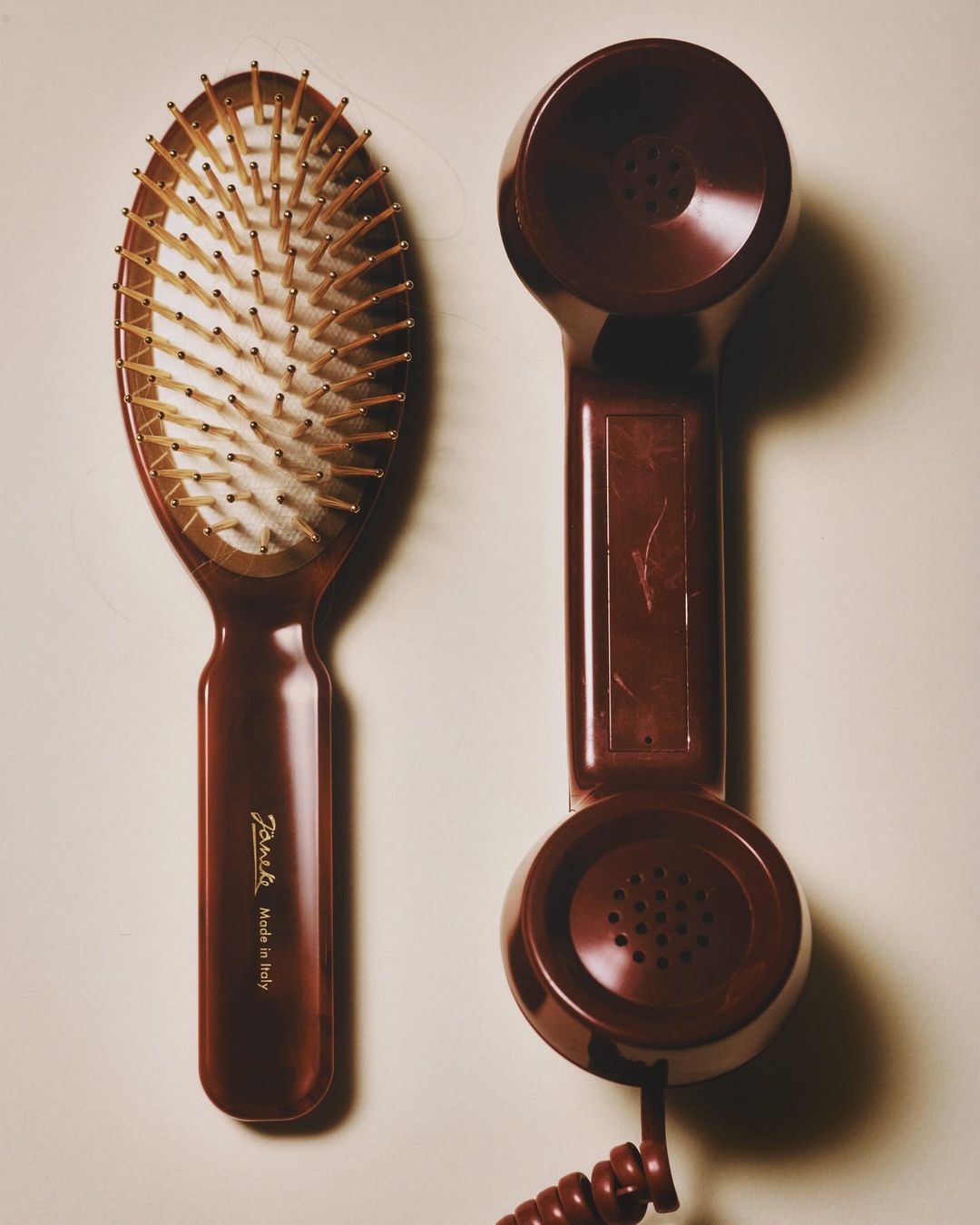 Brown hairbrush with wooden bristles and vintage-style telephone handset on a beige surface in a simple, eye-level product shot.