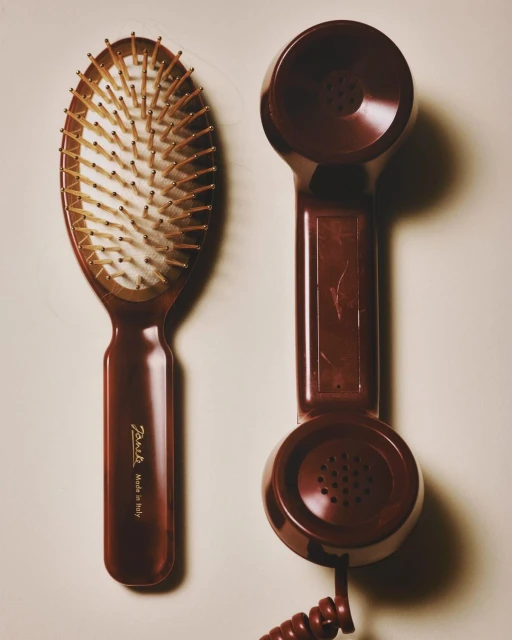 Brown hairbrush with wooden bristles and vintage-style telephone handset on a beige surface in a simple, eye-level product shot.