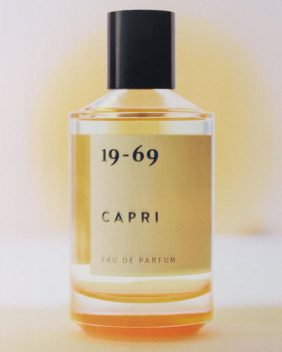 Elegant perfume bottle of 19-69 Capri Eau de Parfum on a soft, gradient background in warm tones. Clean, minimalist composition.