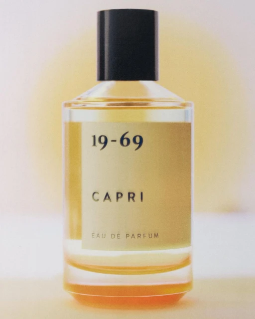 Elegant perfume bottle of 19-69 Capri Eau de Parfum on a soft, gradient background in warm tones. Clean, minimalist composition.