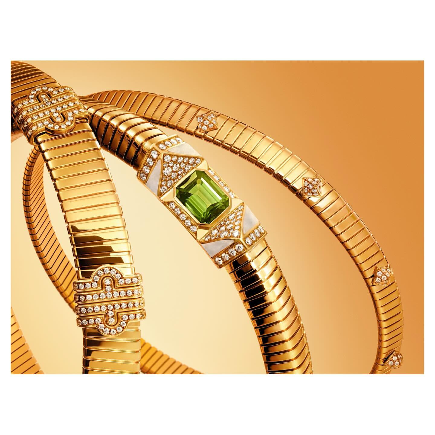 Elevated product shot of gold Bulgari Serpenti Seduttori necklaces featuring diamonds and green gemstones, against a gradient gold backdrop.