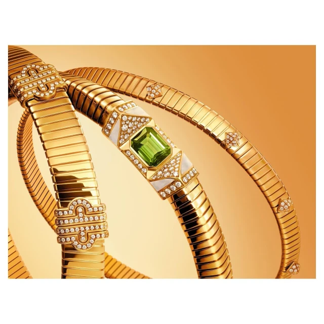 Elevated product shot of gold Bulgari Serpenti Seduttori necklaces featuring diamonds and green gemstones, against a gradient gold backdrop.