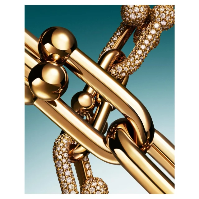 High-angle, close-up studio shot of interlocking gold and diamond chain links against a gradient blue background. Jewelry fashion photography.
