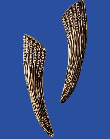 Two curved gold earrings encrusted with small diamonds displayed against a solid blue background.