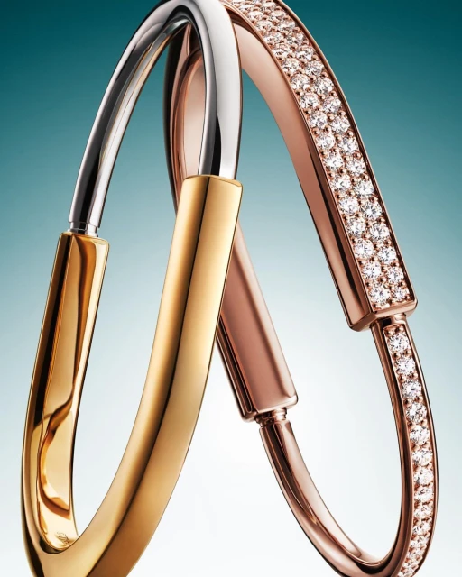 Three metal bangle bracelets in gold, silver, and rose gold with embedded diamonds, overlapping against a blue gradient background.