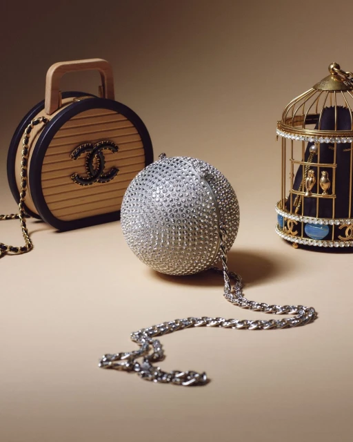 Studio shot showcasing three Chanel purses: a circular wooden handbag, a silver spherical purse with a chain, and a gold birdcage-style purse.