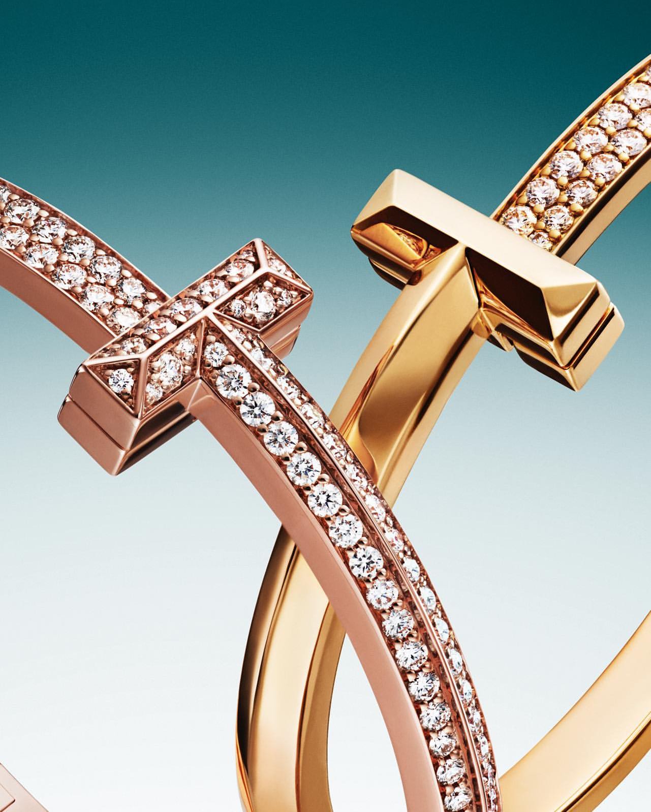 Close-up of interlocking gold and rose gold bracelets embellished with diamonds, showcasing fine jewelry design and craftsmanship on blue gradient.