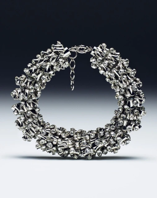 Close-up studio shot of a shiny silver choker necklace with diamond-like embellishments against a graduated gray backdrop.