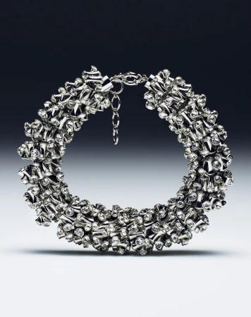Close-up studio shot of a shiny silver choker necklace with diamond-like embellishments against a graduated gray backdrop.