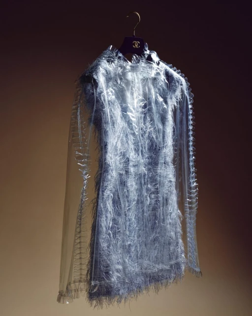 Fringe dress on hanger: a light blue, semi-sheer, fringed cocktail dress hangs against a graduated dark-to-light brown background.