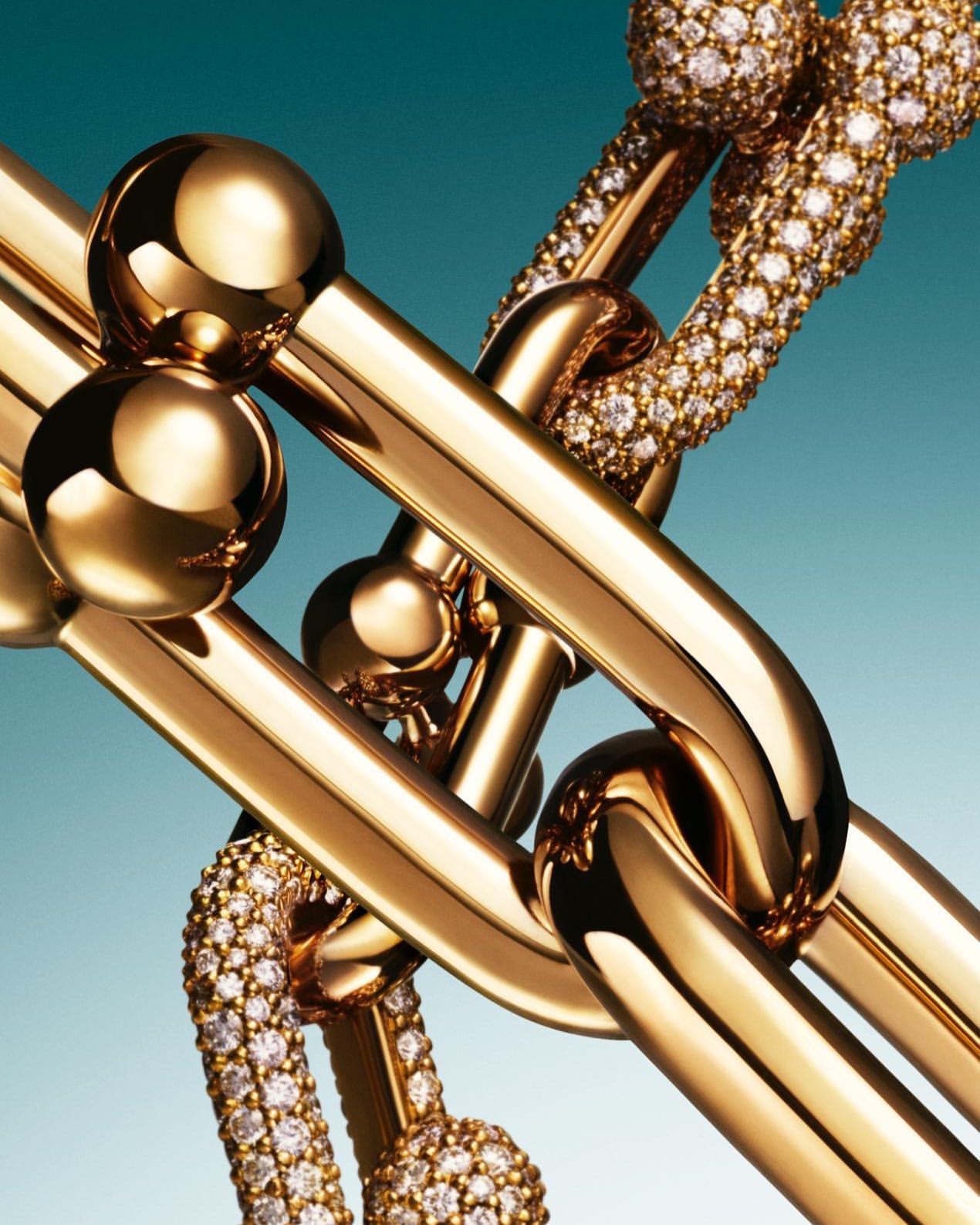 Close-up of interlocking gold chain-link Tiffany bracelets, some with diamond embellishments, against a teal background.