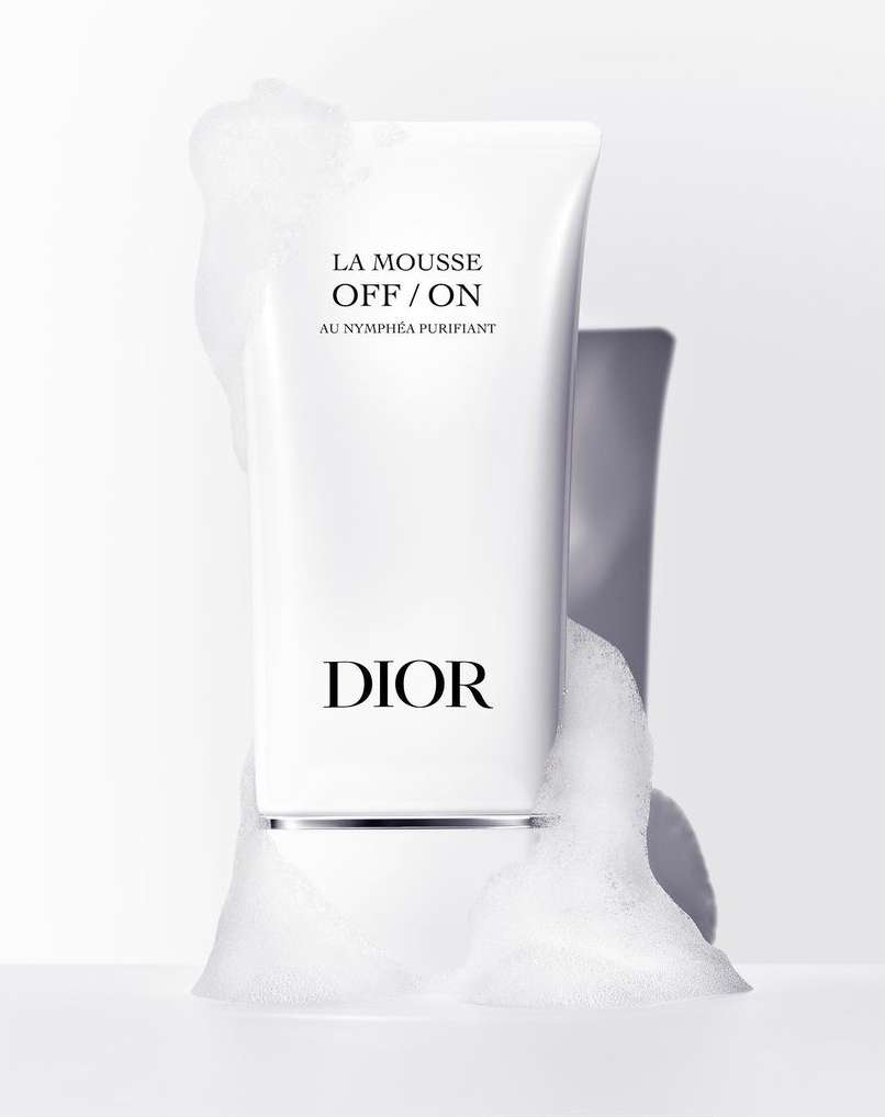 Dior La Mousse OFF/ON facial cleanser in white packaging surrounded by white foam against a soft gradient background.