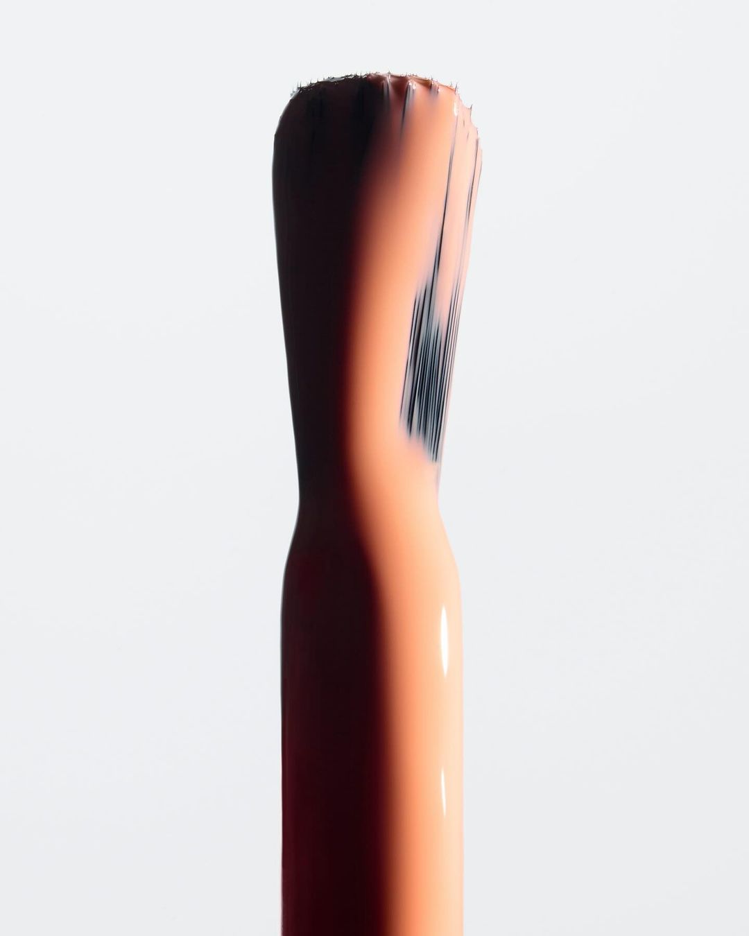 Macro shot of a nail polish brush applicator with peach-colored polish on a stark white background, emphasizing texture and detail.