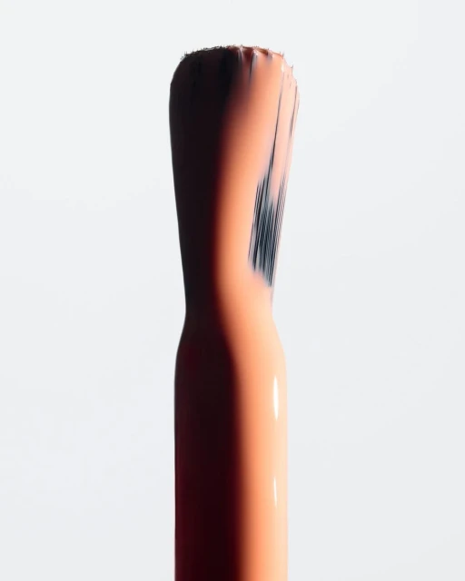 Macro shot of a nail polish brush applicator with peach-colored polish on a stark white background, emphasizing texture and detail.