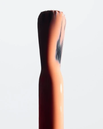 Macro shot of a nail polish brush applicator with peach-colored polish on a stark white background, emphasizing texture and detail.