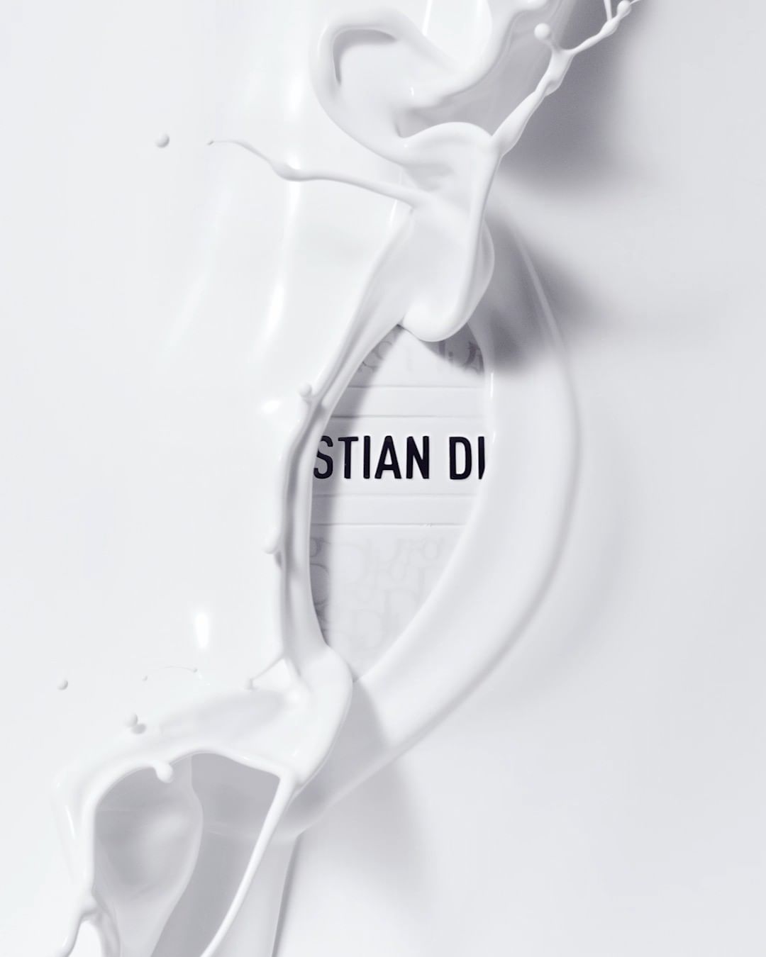 Dynamic splash of white liquid artfully surrounds a 'Christian Dior' sign, set against a bright white background, creating a minimalist aesthetic.