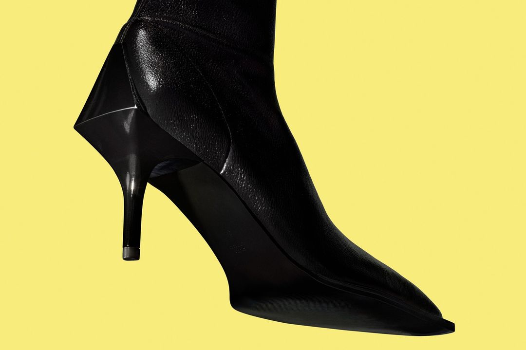 High-fashion black stiletto boot with a geometric heel is isolated against a solid yellow backdrop, showcasing its unique design.