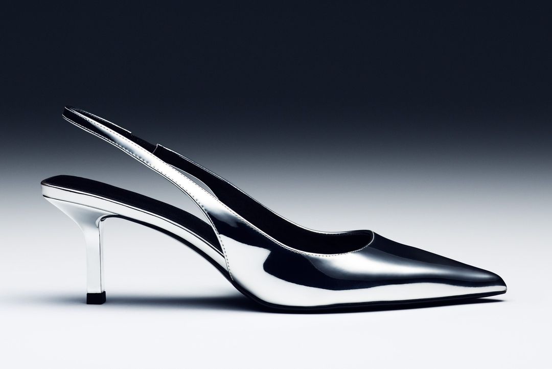 Elegant silver high heel shoe with a pointed toe and slingback strap, set against a graduated grey to black background for a modern fashion look.