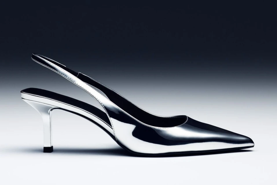 Elegant silver high heel shoe with a pointed toe and slingback strap, set against a graduated grey to black background for a modern fashion look.