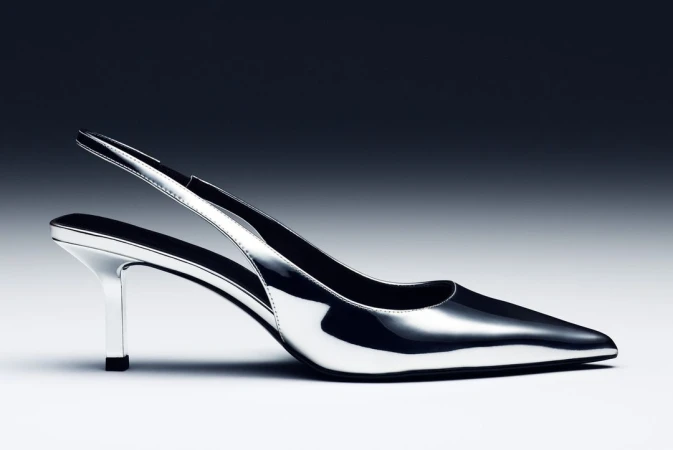 Elegant silver high heel shoe with a pointed toe and slingback strap, set against a graduated grey to black background for a modern fashion look.