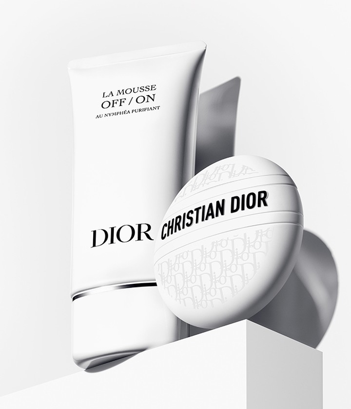 Dior skincare product in a white tube with a white facial puff, set against a clean, minimalist white backdrop and surface.