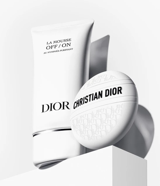 Dior skincare product in a white tube with a white facial puff, set against a clean, minimalist white backdrop and surface.