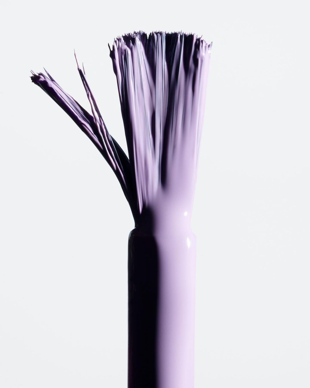 Close-up of a purple-hued nail polish applicator brush with bristles fanned out on a clean white background for beauty product promotion.