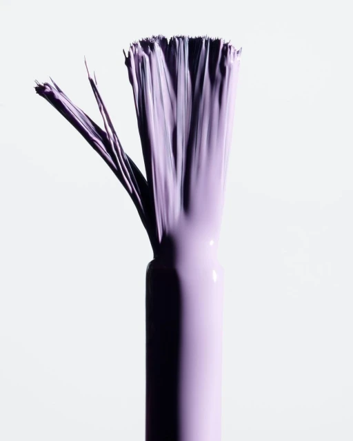 Close-up of a purple-hued nail polish applicator brush with bristles fanned out on a clean white background for beauty product promotion.