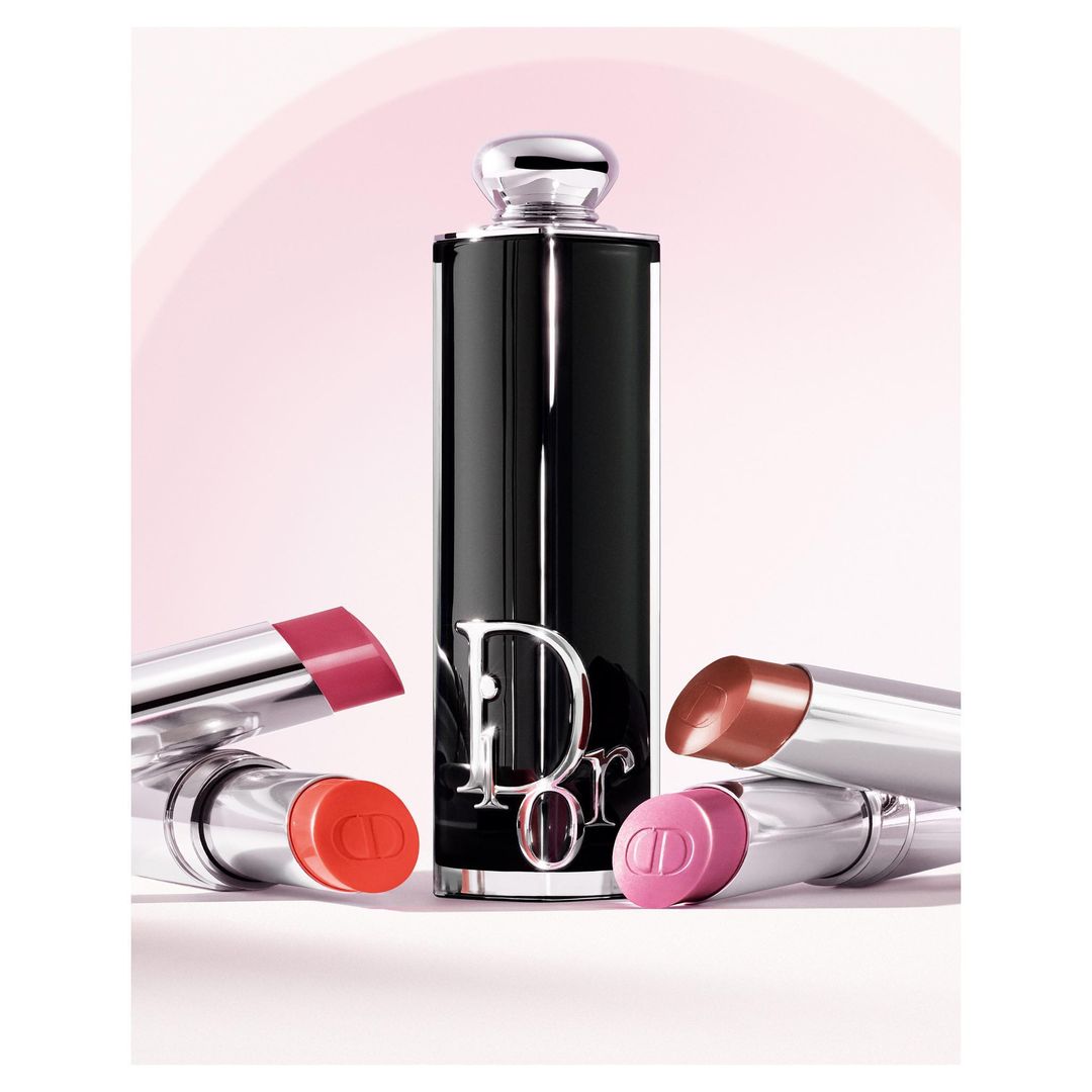 Cosmetics flat lay featuring a Dior lipstick tube and four lipstick refills in pink, red, and brown tones against a soft pink background.