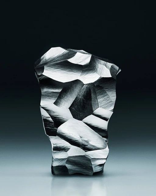 Abstract sculpture with crystalline facets and gray textured surface, contrasted against a dark gray to light gradient background.