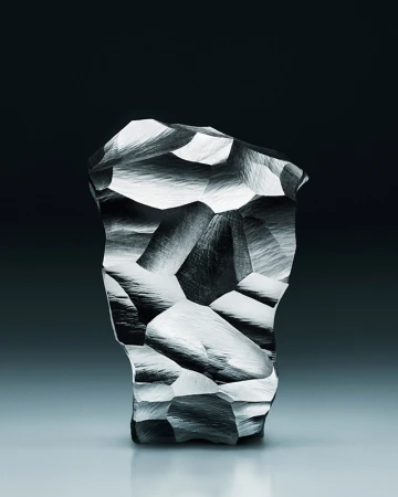 Abstract sculpture with crystalline facets and gray textured surface, contrasted against a dark gray to light gradient background.