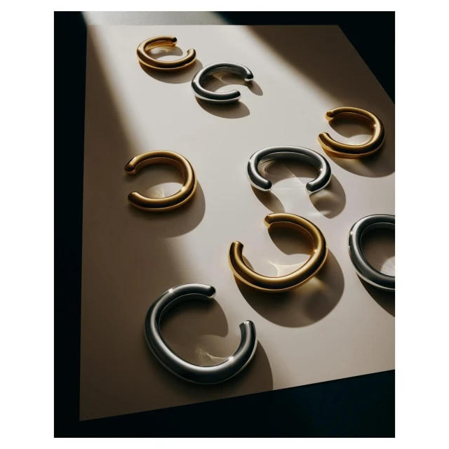 Elegant composition featuring a collection of metallic ear cuffs in gold and silver tones, arranged on a surface with dark accents. Studio shot.