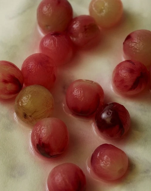 Close-up of glistening red and pale green grapes, displaying their fresh, natural colors and plump, juicy texture on a plain background.