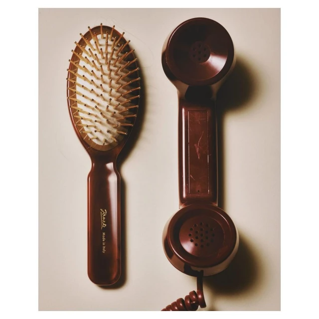 Still life photograph of a brown hairbrush and a vintage brown telephone receiver against a neutral background, lit by soft light.