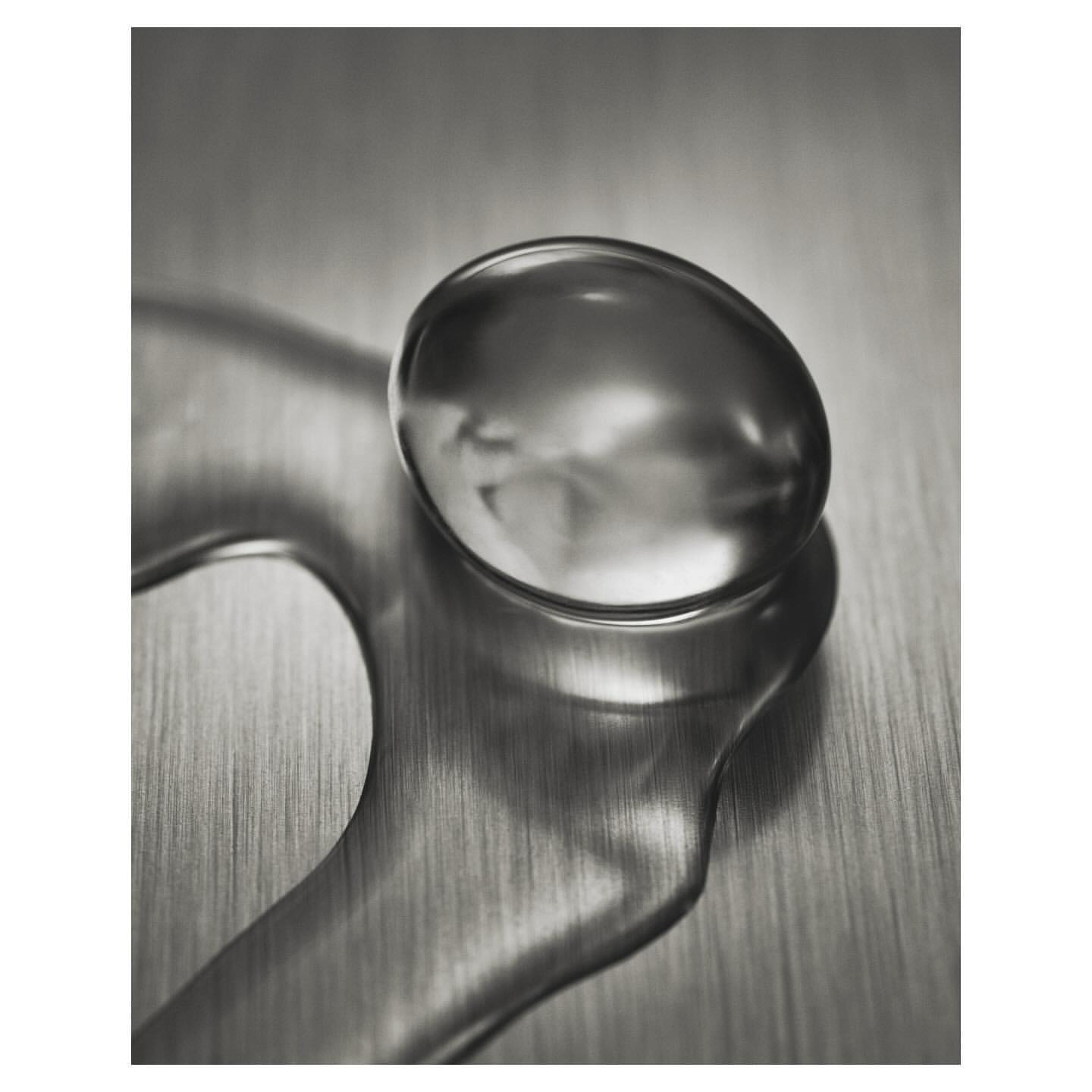 Macro shot of a water droplet with unique shape and reflection on a metallic surface with blurred background; studio lighting.