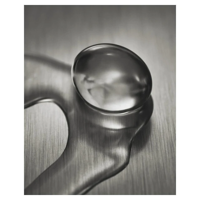 Macro shot of a water droplet with unique shape and reflection on a metallic surface with blurred background; studio lighting.