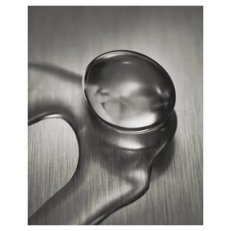 Macro shot of a water droplet with unique shape and reflection on a metallic surface with blurred background; studio lighting.